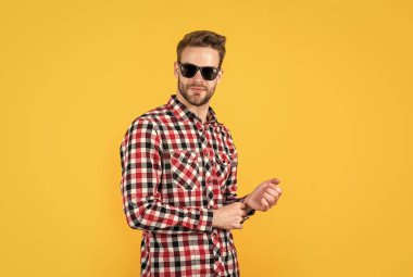 Moda görünüyor. İyi bakımlı bir saç stili. Erkek güzellik ve moda. Sakallı adam için kareli gömlek. Tıraşsız, güneş gözlüklü yakışıklı adam. Kuaför konsepti. Genç ve kendinden emin