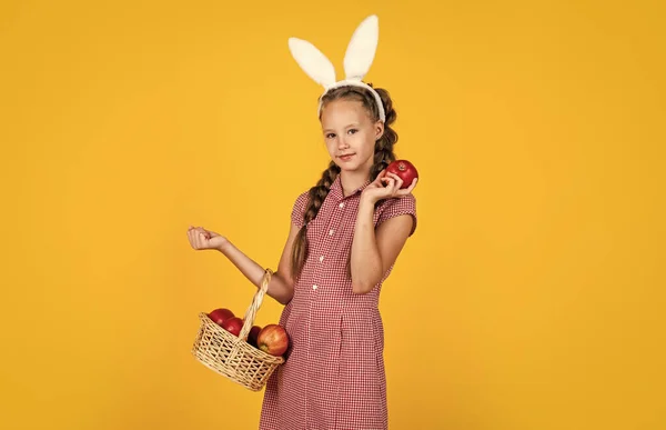 Szczęśliwa dziewczyna trzyma jabłka z ogrodu. Dzieciak królik trzyma kosz z owocami. Dziecko nosi królicze uszy. Wiosenna zabawa. Wesołych Świąt. Zaczęło się polowanie. szczęście z dzieciństwa. Przygotowania do Wielkanocy — Zdjęcie stockowe