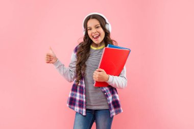 Kulaklıkla müzik dinleyen mutlu bir çocuk. Pembe arka planda çalışma kitabı var.