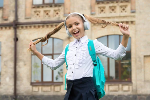 Happy school girl in uniform having fun listening to music in headphones and holding hair — Stock Photo, Image