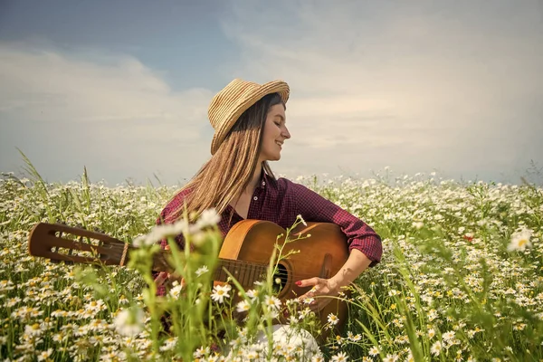 So happy. beautiful woman play guitar among chamomile flower field. summer or spring nature. seasonal beauty. young girl in hat play country music in meadow. vacation. sense of freedom — Stock Photo, Image