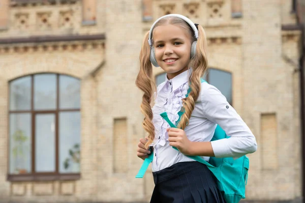 Happy school leerling in uniform luisteren naar audio cursus in hoofdtelefoon, onderwijs — Stockfoto