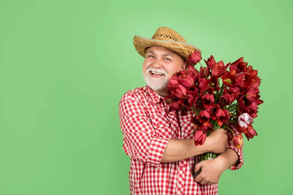 戴着帽子的快乐的退休老人拿着绿色背景的春天郁金香花。复制空间 — 图库照片