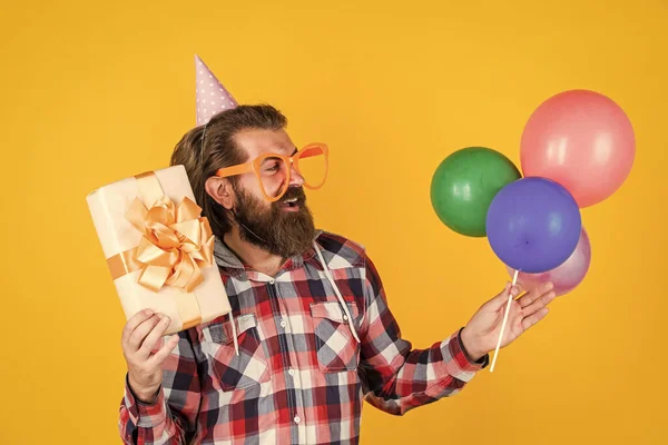 Havalı saç stili olan şık sakallı adam kareli gömlek giyiyor parti balonları ve hediye kutusu, doğum günü hediyesi. — Stok fotoğraf