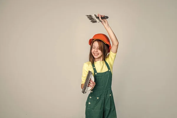 彼女は仕事が好きだ。作業道具を使って。ヘルメットを着た10代の女の子とヘラでボイラースーツ。子供は硬い帽子をかぶる。建設現場の子供のビルダー。労働者技術者。建築家のワークショップです。改修と修理 — ストック写真