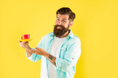 Mutlu sakallı adam sarı arka planda sabah kahvesini sunar.
