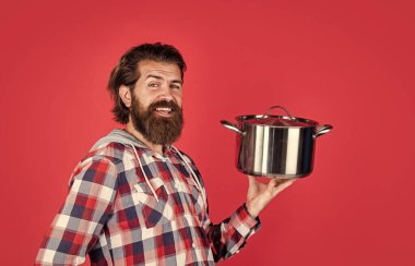 Kareli gömlekli, olgun, yakışıklı bir adam yemek pişirmek için tava tutuyor.