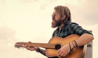 Şık saçlı, akustik gitar çalan yakışıklı sakallı adam.