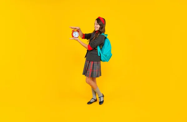 Gelukkig kind in school uniform en rugzak houden wekker op gele achtergrond, student — Stockfoto