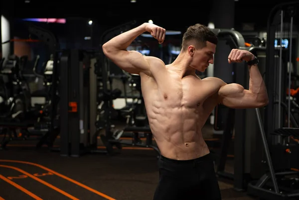 Starker Mann mit durchtrainiertem Oberkörper, der die Armmuskeln anspannt, steht in Doppelbizeps-Pose im Fitnessstudio, Kraft — Stockfoto