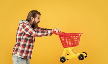 Havalı saç stili olan şık sakallı adam kareli gömlek giyer alışveriş arabası alır.