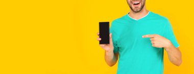 Kesilmiş adam telefon ekranını sunuyor. Adam sarı arka planda akıllı telefonu işaret ediyor..