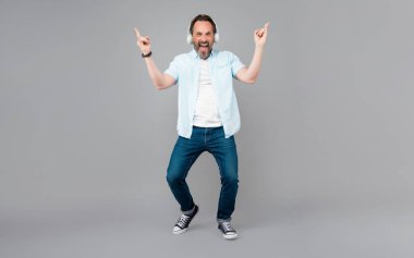 Mutlu eski rockçı rock müzik eşliğinde şarkı söyler kulaklıkla çalar boynuz işaretleri gri arka plan, şarkı