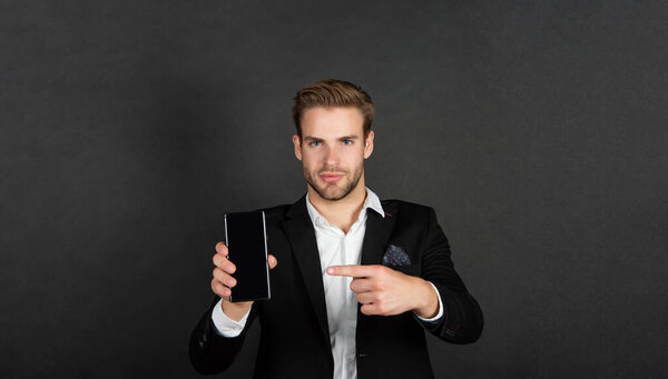 Professional manager in suit pointing finger at mobile device dark background copy space, phone