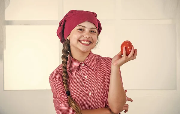 요리사 유니폼을 입은 십 대 소녀가 웃으며 야채와 토마토를 요리하는 모습 — 스톡 사진
