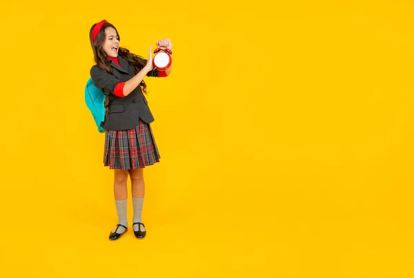 Niño infeliz en uniforme escolar con mochila con despertador alto en espacio de copia, tiempo. —  Fotos de Stock