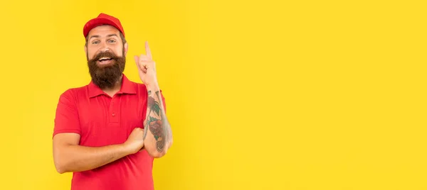 Entregador feliz em casuais boné vermelho e tshirt mantendo o dedo levantado espaço cópia, ideia — Fotografia de Stock