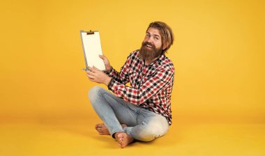 Kareli gömlekli, modaya uygun saç stili olan beyaz bir hippi klasör kâğıdına notlar yazıyor.