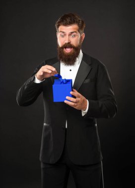 Smokinli, papyonlu, siyah arka planda, hediye kutusuyla resmi kıyafetli, hayret verici bir adam. Boks günü