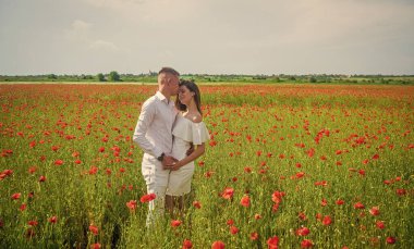 Aşık mutlu bir çift romantik bir günde, gelincik çiçeğinin güzel tarlasında yürüyor, romantik bir randevu