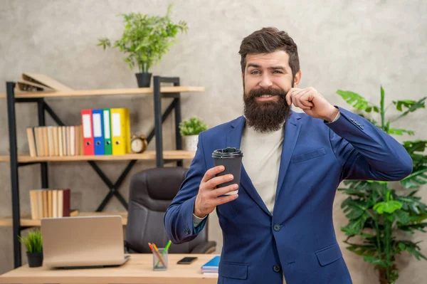 Uomo d'affari barbuto sorridente bere caffè da asporto in ufficio con spazio copia, caffè del mattino — Foto Stock