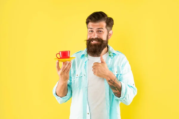 Heureux homme barbu boire café matin montrant pouce vers le haut sur fond jaune, tasse de café — Photo
