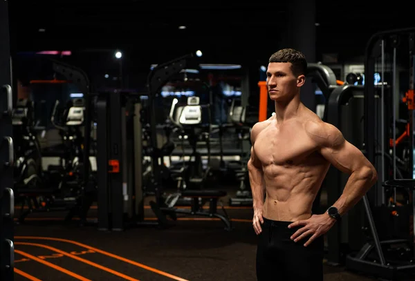 Sportlicher Mann mit muskulösem Oberkörper, stehend mit Armen akimbo im Fitnessstudio, Sportler — Stockfoto