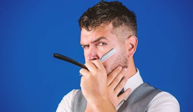 Kuaför keskin tehlike ustura ile tıraşsız hippi. Berber Kuaför Salonu. İpuçları bakım Kuaför sakal. Erkek yelek papyon ile usturanın mavi arka plan tutun. Kuaför sanat kavramı