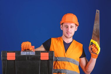 İşçi, repairer, gülümseyen yüz taşıyan araç, onarım için kopya alanı hazır üzerinde tamirci. Marangoz kavramı. Kask, kask içinde adam araç kutusu taşır ve el testeresi, mavi arka plan tutar