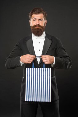 Smokin giymiş, papyon takan, siyah arka planda, alışveriş çantalı bir adam. Alışveriş satışı. Boşluğu kopyala