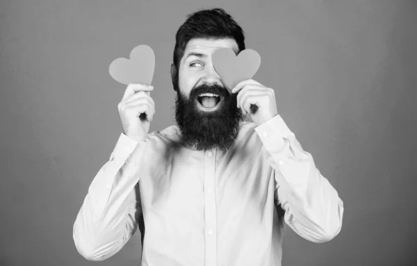 Feliz día de San Valentín. Hombre barbudo ocultando el ojo con el corazón rojo. Hipster sosteniendo corazones pequeños. Sexy hombre de San Valentín con tarjetas en forma de corazón. La fiesta del amor y el romance. El amor es la clave de la felicidad —  Fotos de Stock