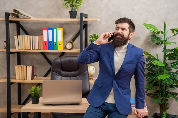 Onnellinen pukumies puhuu matkapuhelimella, istuu toimistossa, kännykkä — kuvapankkivalokuva