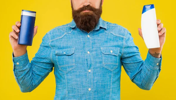 Hombre barbudo brutal recortado elegir botella acondicionador de pelo, presentando artículos de tocador. — Foto de Stock