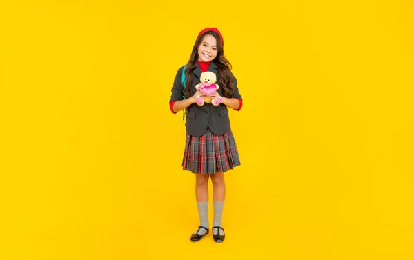 Gelukkig tiener meisje in uniform met schooltas houden speelgoed op gele achtergrond, onderwijs — Stockfoto