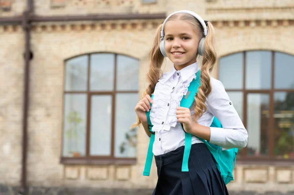 Щаслива шкільна дитина в уніформі прослуховування аудіокурсу в навушниках, освіта — стокове фото