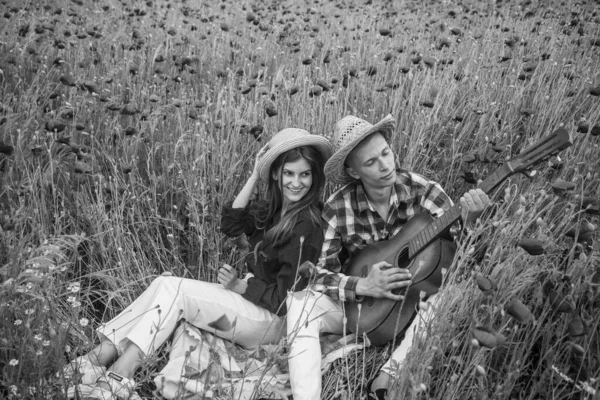 Romantyczna para grająca na gitarze na polu z czerwonymi kwiatami, letnie wakacje — Zdjęcie stockowe