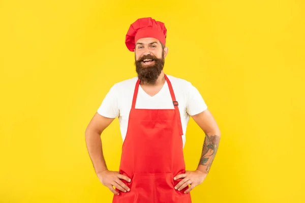 Happy man in rode toque en schort met armen akimbo gele achtergrond, chef-kok — Stockfoto