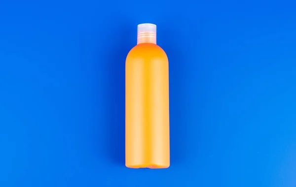 Botella de champú naranja sobre fondo azul, artículos de tocador — Foto de Stock