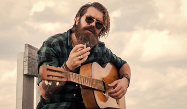 Müzik aleti olan erkek gitarist. Country müzik konsepti. Sakallı adam akustik gitar çalar. Sıradan bir adam insani duygularını ifade eder. Uzun saçlı hippi ve bıyıklı gitarist. Ritmi oynat