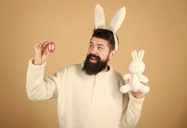 Easter activities concept. Weirdo concept. Celebrate Easter. Guy bearded hipster weird bunny with long white ears beige background. Easter rabbit. Man wearing rabbit suit. Funny bunny man soft ears