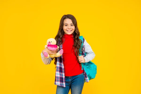 Criança feliz estilo casual com mochila e brinquedo no fundo amarelo, educação — Fotografia de Stock