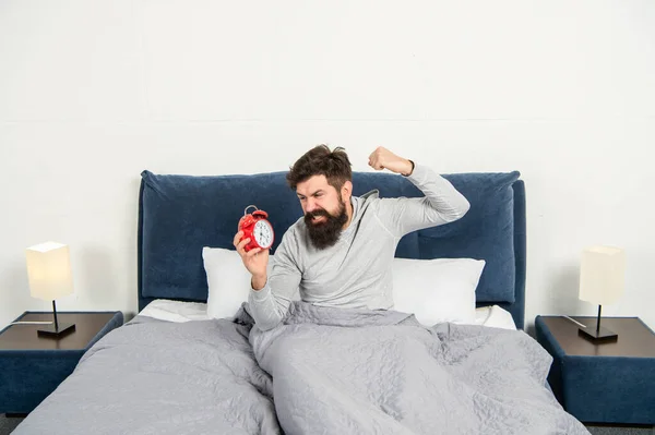 Homme en colère qui figurait avec réveil étant au lit le matin, dormait trop — Photo