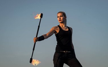 Seksi kadın ateş manipülatörü alevli baton çeviriyor akşam mavi gökyüzü, tehlikeli