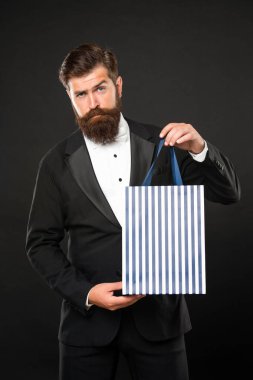Smokinli papyonlu adam siyah arka planda alışveriş çantasını sunuyor. Sevgililer Günü. Boşluğu kopyala.