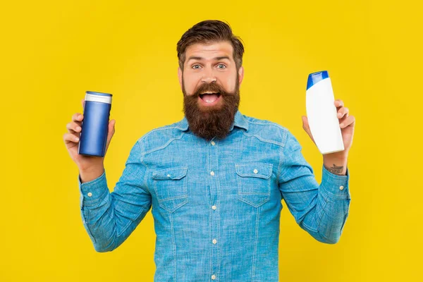 Stupito uomo barbuto brutale scegliendo bottiglia condizionatore per capelli, presentando articoli da toeletta. — Foto Stock