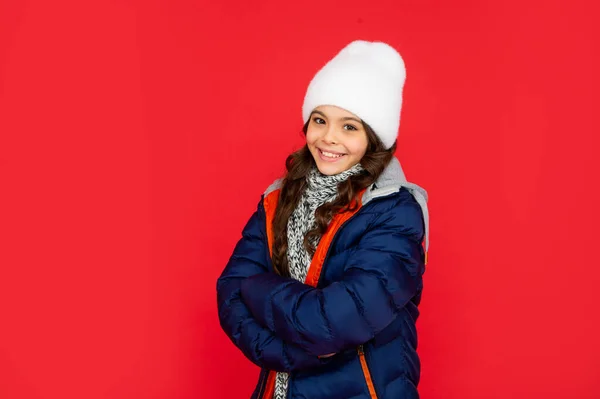 Vintermode. Glada unge med lockigt hår i puffar jacka och hatt. tonåring flicka på röd bakgrund. — Stockfoto