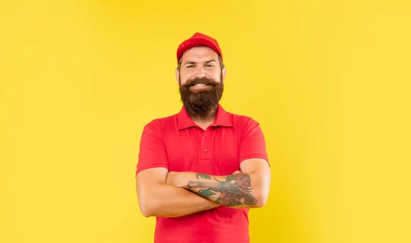 快乐自信的男人，头戴休闲红帽，头戴短衫，双手交叉在黄色背景上，送货员 — 图库照片