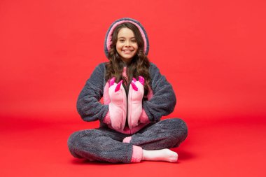 Rahat pijamalı mutlu çocuk kırmızı arka planda komik terlikler tutuyor, çocukluk.