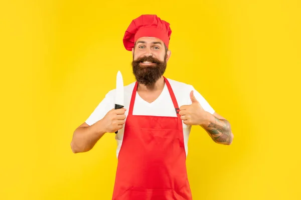 Glücklicher Mann in roter Schürze und Haube, Daumen haltend Küchenmesser gelben Hintergrund, Koch — Stockfoto