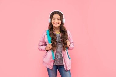 Sırt çantalı mutlu genç kız pembe arka planda kulaklık takıyor, okul...